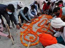 Personas entierran hoy el cuerpo de un familiar que no murió por COVID-19, en una tumba en la arena junto a la orilla del río Ganges, en Prayagraj. La policía dijo que ya no permitirá entierros en la ribera. AP/R. Kumar Singh