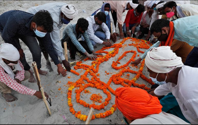 Personas entierran hoy el cuerpo de un familiar que no murió por COVID-19, en una tumba en la arena junto a la orilla del río Ganges, en Prayagraj. La policía dijo que ya no permitirá entierros en la ribera. AP/R. Kumar Singh