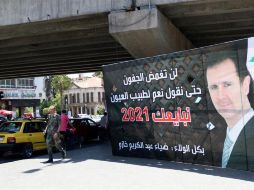 Varios peatones pasan junto a un cartel electoral que muestra al presidente sirio, Bachar Al Assad, en la víspera de las elecciones presidenciales, en Damasco. EFE/Y. Badawi