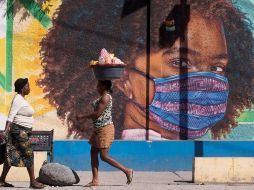 Dos mujeres caminan frente a un mural alusivo al uso del tapabocas por el coronavirus, en Puerto Príncipe, Haití. EFE/O. Barría
