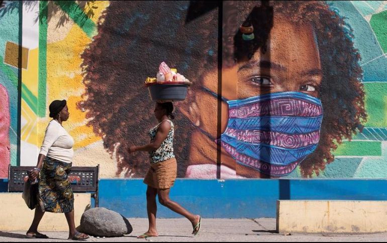 Dos mujeres caminan frente a un mural alusivo al uso del tapabocas por el coronavirus, en Puerto Príncipe, Haití. EFE/O. Barría