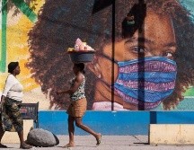 Dos mujeres caminan frente a un mural alusivo al uso del tapabocas por el coronavirus, en Puerto Príncipe, Haití. EFE/O. Barría