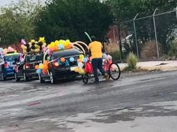 En la publicación se puede ver a un hombre formado en la fila de coches con su triciclo adornados de globos de colores. Facebook / T. Coronel