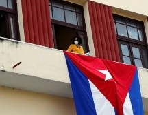 Una mujer sale al balcón donde se expone una bandera cubana, este martes en La Habana. EFE/E. Mastrascusa