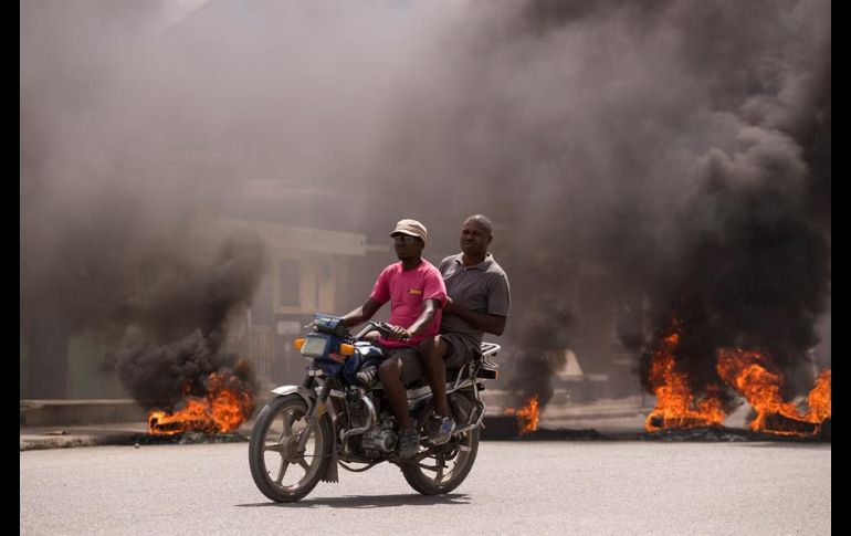 Dos hombres en motocicleta pasan frente a una barricada en llamas durante una jornada de protestas en Cap-Haitien, Haití. EFE/O. Barría