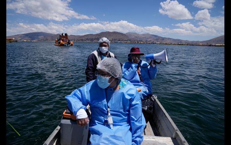 La obstetra Deysi Barriga anuncia la llegada del bote a las islas, mientras que el técnico Sebastián Quispe dirige la pequeña nave que transporta un recipiente con vacunas de Pfizer. AP/M. Mejía