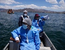 La obstetra Deysi Barriga anuncia la llegada del bote a las islas, mientras que el técnico Sebastián Quispe dirige la pequeña nave que transporta un recipiente con vacunas de Pfizer. AP/M. Mejía