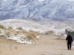 Una persona camina junto al muro fronterizo con EU mientras las montañas están con nieve en Ciudad Juárez, Chihuahua. EFE/L. Torres
