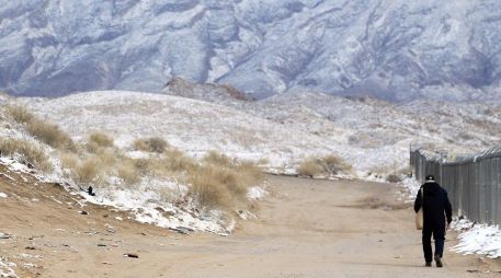 Una persona camina junto al muro fronterizo con EU mientras las montañas están con nieve en Ciudad Juárez, Chihuahua. EFE/L. Torres