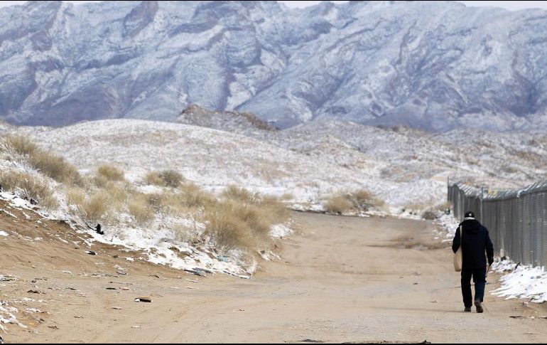 Una persona camina junto al muro fronterizo con EU mientras las montañas están con nieve en Ciudad Juárez, Chihuahua. EFE/L. Torres