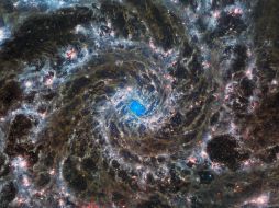 La imagen muestra los brillantes apéndices blancos, rojos, rosas y azul claro de la galaxia que se arremolinan alrededor de un centro azul brillante. AFP/NASA
