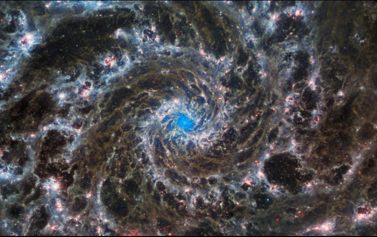 La imagen muestra los brillantes apéndices blancos, rojos, rosas y azul claro de la galaxia que se arremolinan alrededor de un centro azul brillante. AFP/NASA