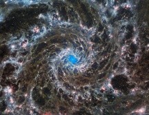 La imagen muestra los brillantes apéndices blancos, rojos, rosas y azul claro de la galaxia que se arremolinan alrededor de un centro azul brillante. AFP/NASA