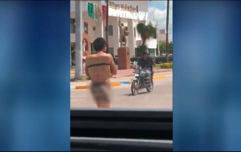 El joven, con los brazos atados y ocultándose el rostro, el cual solo llevaba puestos 