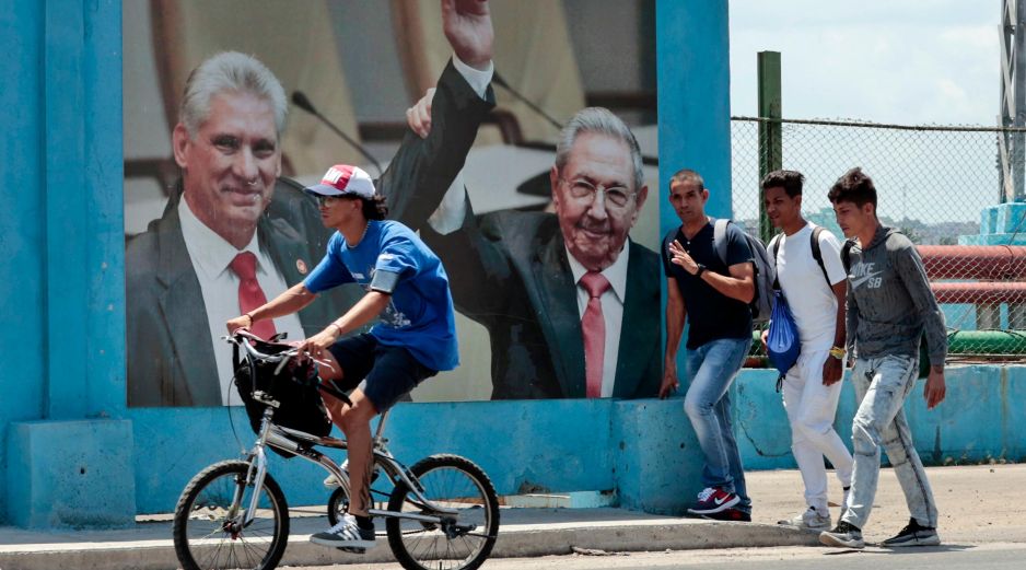 Un grupo de hombres caminan frente a una fotografía del presidente de la República de Cuba Miguel Díaz-Canel junto a Raúl Castro, en La Habana. EFE/E. Mastrascusa