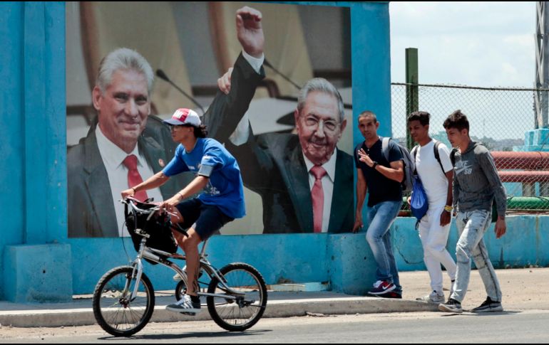 Un grupo de hombres caminan frente a una fotografía del presidente de la República de Cuba Miguel Díaz-Canel junto a Raúl Castro, en La Habana. EFE/E. Mastrascusa