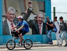 Un grupo de hombres caminan frente a una fotografía del presidente de la República de Cuba Miguel Díaz-Canel junto a Raúl Castro, en La Habana. EFE/E. Mastrascusa