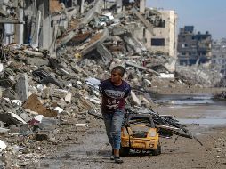 Un niño acarrea metales para reciclar sobre un carro de juguete, con los primeros charcos de lluvia como amenaza. EFE/M. Saber