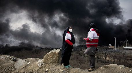 Dos mujeres de la Sociedad de la Media Luna Roja iraní permanecen de pie mientras una densa columna de humo proveniente de un ataque estadounidense-israelí contra una instalación de almacenamiento de petróleo en Teherán, Irán. AP/V. Salemi