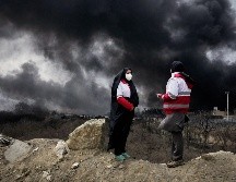 Dos mujeres de la Sociedad de la Media Luna Roja iraní permanecen de pie mientras una densa columna de humo proveniente de un ataque estadounidense-israelí contra una instalación de almacenamiento de petróleo en Teherán, Irán. AP/V. Salemi