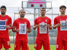 Jugadores iraníes cantan el himno nacional, sosteniendo fotografías de niños presuntamente asesinados en ataques parte de la guerra que EU e Israel sostienen contra Irán. AP / Riza Ozel
