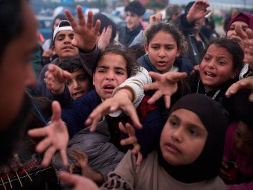 Familias desplazadas extienden las manos mientras esperan a recibir donativos de alimentos en un campamento después de huir de los bombardeos israelíes en el sur de Líbano. AP/E. Morenatti