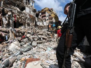 Un hombre armado monta guardia mientras una excavadora retira los escombros de un edificio parcialmente destruido tras un ataque aéreo israelí, durante una visita de prensa organizada por la oficina de prensa de Hezbolá, en Líbano. EFE/W. HAMZEH