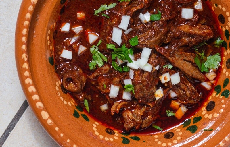 La birria se sirve en un plato hondo, bañada con su propio consomé bien caliente, y se adorna con cebolla picada, cilantro fresco y un chorrito de limón.&nbsp;ESPECIAL / CANVA