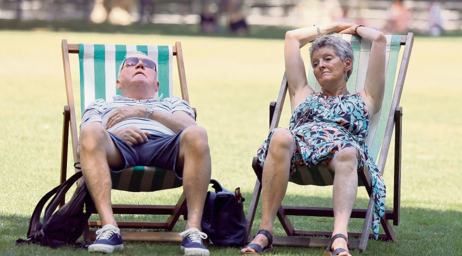 Dos ingleses buscan descansar en un parque público, ante las inusuales condiciones que enfrenta la ciudad. EFE