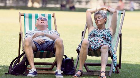 Dos ingleses buscan descansar en un parque público, ante las inusuales condiciones que enfrenta la ciudad. EFE