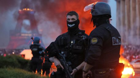 Un automóvil arde y estallan fuegos artificiales mientras la policía observa a los aficionados del PSG celebrar en París. AP/T. Padilla