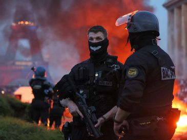 Un automóvil arde y estallan fuegos artificiales mientras la policía observa a los aficionados del PSG celebrar en París. AP/T. Padilla