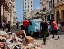 Varias personas empujan un coche clásico americano averiado junto a un montón de basura en La Habana. AP/J. Banos