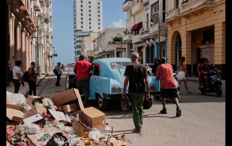 Varias personas empujan un coche clásico americano averiado junto a un montón de basura en La Habana. AP/J. Banos