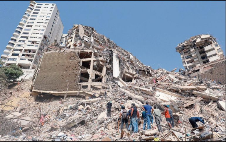 Un grupo de personas contemplan los escombros de edificios derrumbados tras el sismo. XINHUA