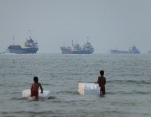 Dos niños de pie en aguas poco profundas con flotadores de espuma, mientras se ven buques de carga y otras embarcaciones en el estrecho de Ormuz, frente a Bandar Abbas, Irán. AP/A. Khorgooi