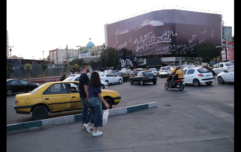 Una mujer y un hombre cruzan a unos metros de un enorme mural que muestra a Donald Trump en un ataúd, acompañada de una frase en persa que dice: 