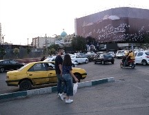 Una mujer y un hombre cruzan a unos metros de un enorme mural que muestra a Donald Trump en un ataúd, acompañada de una frase en persa que dice: 