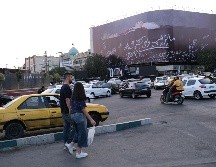 Una mujer y un hombre cruzan a unos metros de un enorme mural que muestra a Donald Trump en un ataúd, acompañada de una frase en persa que dice: 
