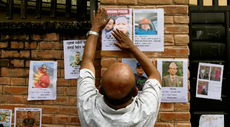 Un hombre cuelga la fotografía de uno de sus conocidos, con la esperanza de que sea identificado con vida por el gobierno nepalí. EFE/N. Shrestha