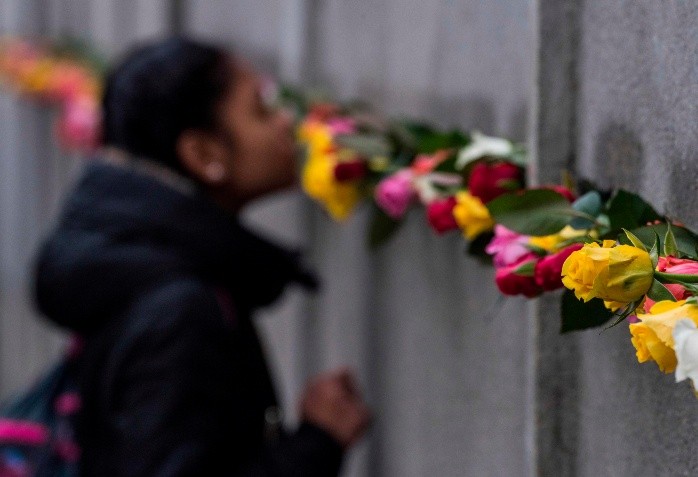 A schoolgirl peers through a slit in the back wall at the Berlin Wall - A schoolgirl peers through a slit in the back wall at the Berlin Wall Memorial where flowers have been placed in a crack on November 9, 2017 during the commemorations to mark the 28th anniversary of the fall of the Berlin Wall.  / AFP / John MACDOUGALL GERMANY-HISTORY-WALL-COMMEMORATION