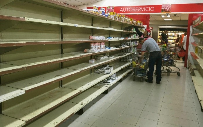 Trabajadores de un supermercado ordenan los estantes, tras la llegada de cientos de personas a comprar la mercancía a la que se le bajó el precio. EFE
