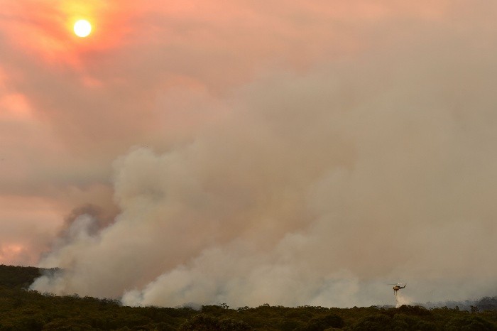 TOPSHOT - A helicopter drops water onto a large bushfire in Bargo, 150km southwest of Sydney on December 19, 2019.  A state of emergency was declared in Australia's most populated region on December 19 as an unprecedented heatwave fanned out-of-control bushfires, destroying homes and smothering huge areas with a toxic smoke. / AFP / Peter PARKS TOPSHOTS-TOPSHOT-AUSTRALIA-FIRE-CLIMATE-HEALTH-ENVIRONMENT