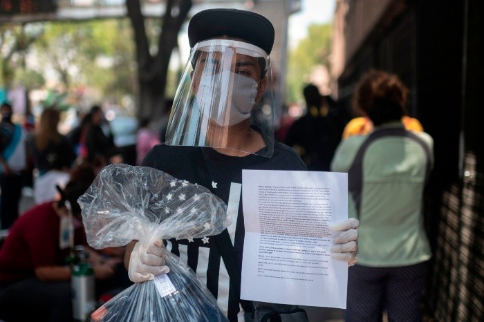 Marco Antonio Olivares wears a face mask and shield as he shows a personal message he sends in a package to a relative infected with COVID-19 who remains in La Raza medical center, in Mexico City on April 29, 2020. Handwritten notes are the thread of communication between patients infected with coronavirus and their relatives in the Mexican capital. / AFP / PEDRO PARDO MEXICO-HEALTH-VIRUS-TO GO WITH AFP STORY BY NATALIA CANO