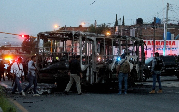 Members of the State Prosecutor's Office and Municipal Police guard the area where gang members set a bus on fire blocking a highway to prevent authorities from chasing them while they were clashing with another gang, in Zapopan, Jalisco State, Mexico, on August 9, 2022. According to the authorities, no one was injured. (Photo by ULISES RUIZ / AFP)